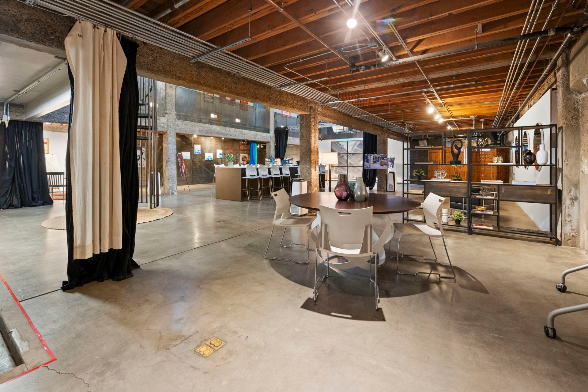 Main floor work area with a round meeting table, blackout drapes, exposed timber ceiling and open shelving