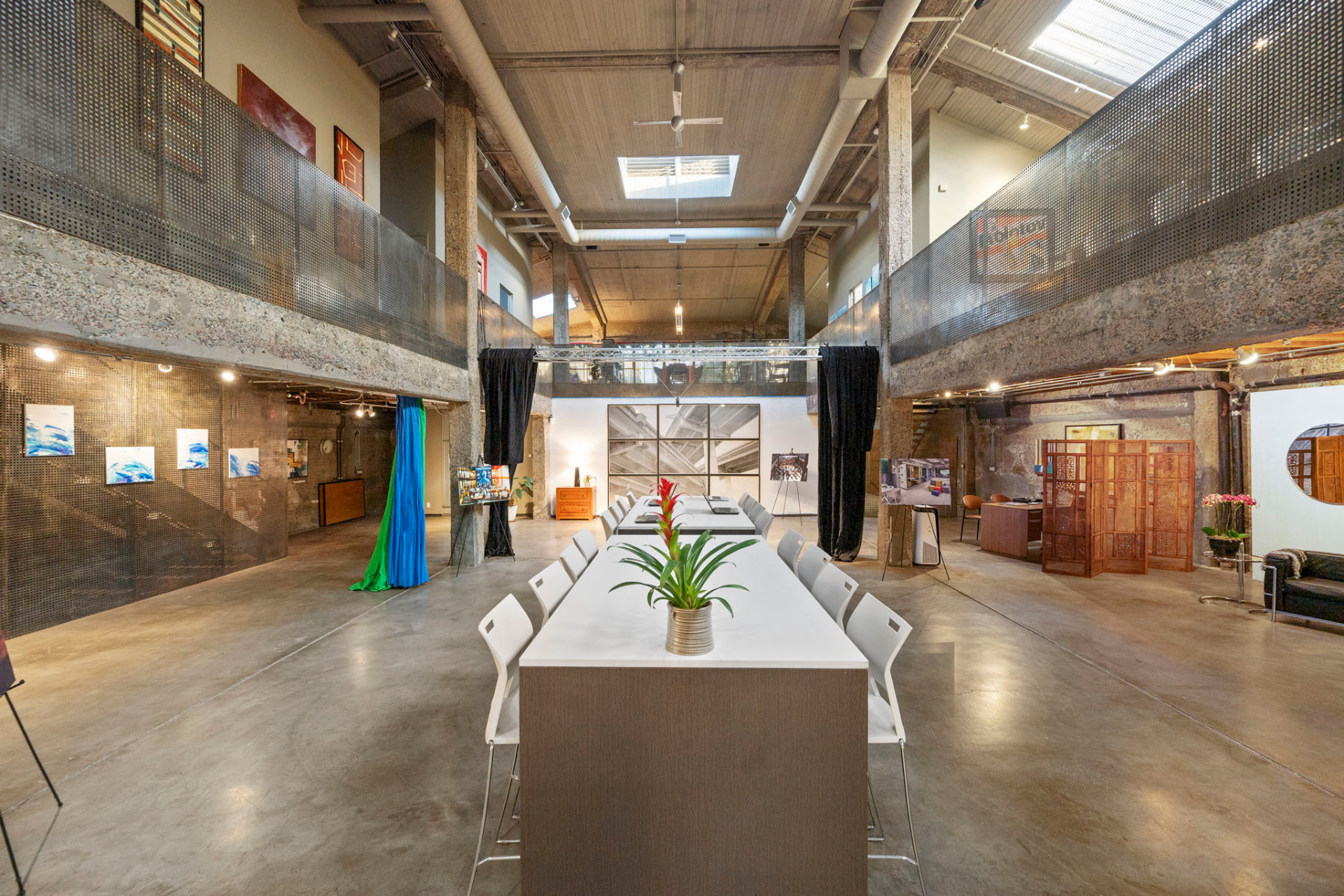Double-height main floor at 270 14th Street with concrete columns, perforated steel mezzanine railings and a long communal table beneath skylights