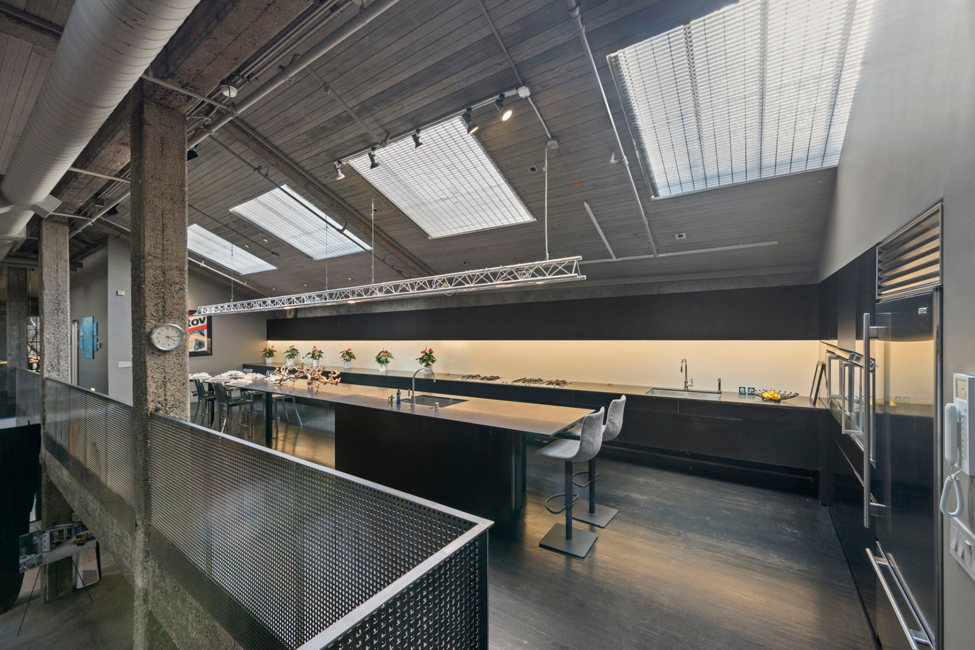 Full view of the kitchen with black cabinetry, a run of skylights overhead and a lighting truss above the island